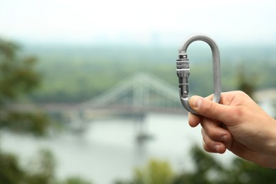 Photo of Man holding metal carabiner outdoors, closeup. Space for text