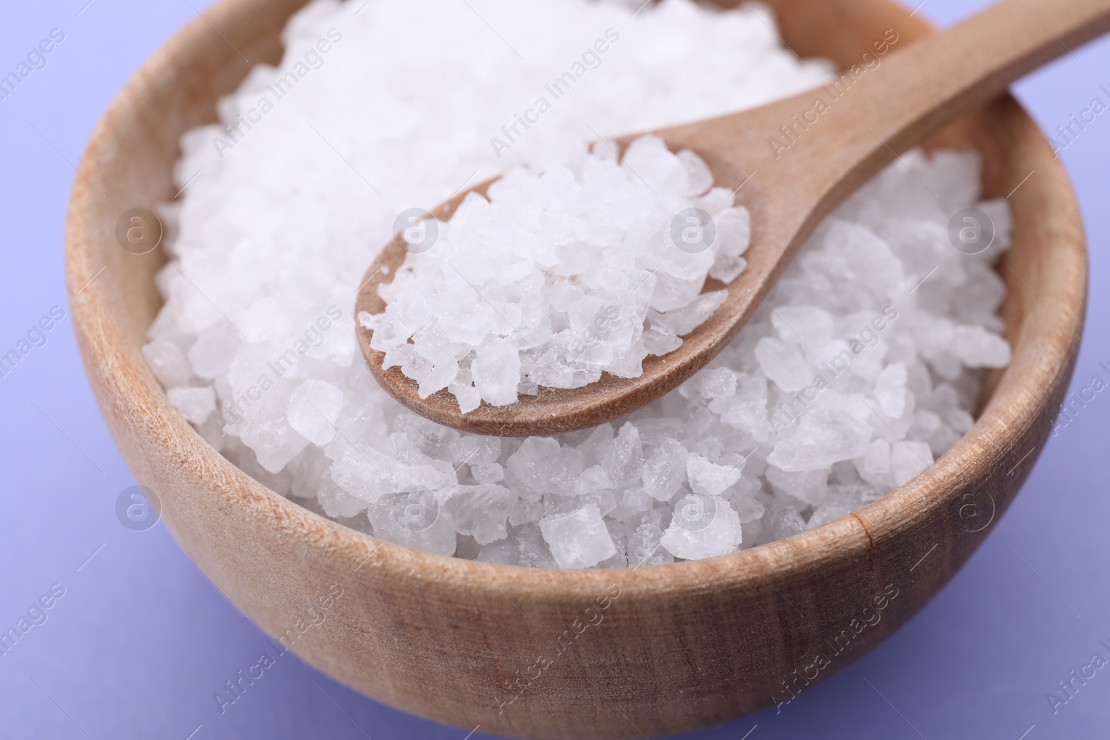 Photo of Bowl and spoon with sea salt on violet background, closeup