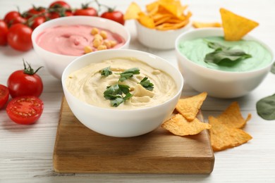 Photo of Different kinds of tasty hummus, nachos and ingredients on white wooden table