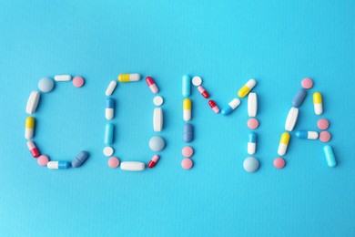 Word Coma made of pills on light blue background, flat lay