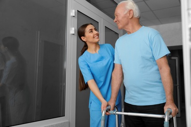 Nurse assisting senior patient with walker in hospital hallway