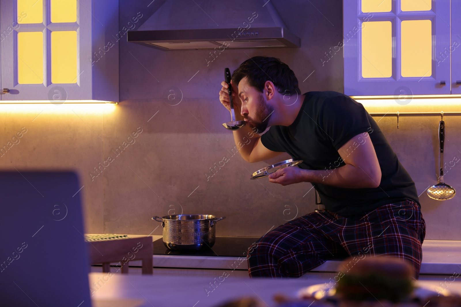 Photo of Man eating soup in kitchen at night. Bad habit