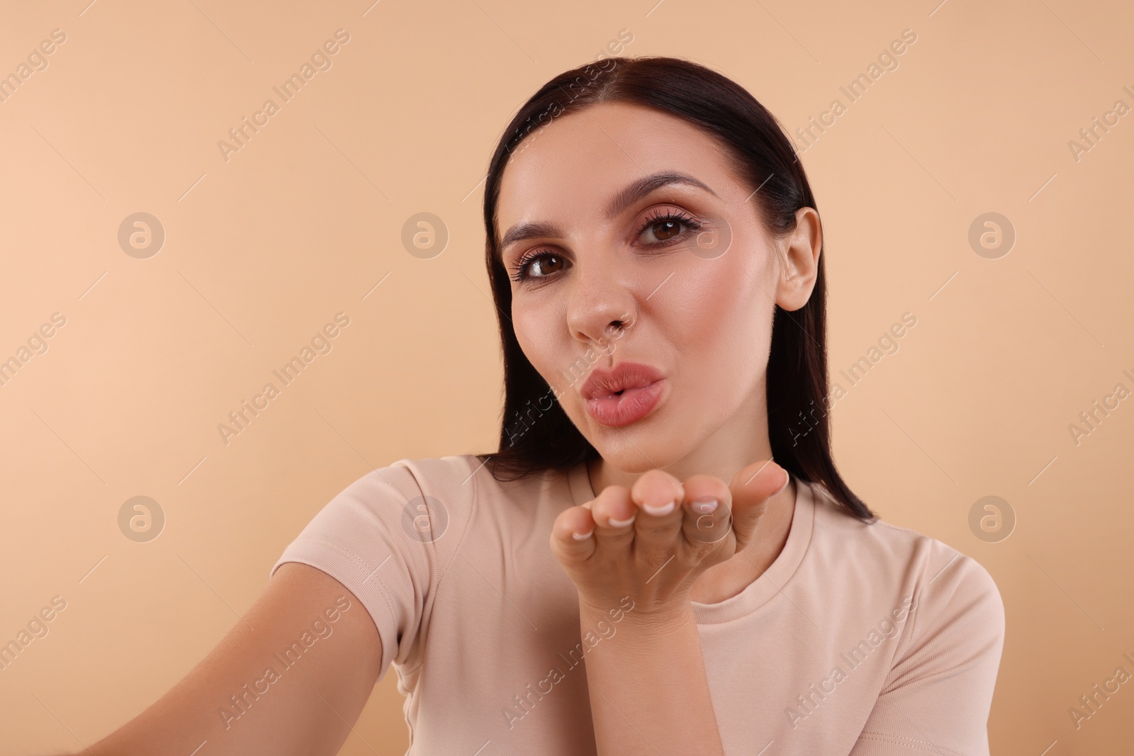 Photo of Young woman taking selfie and blowing beige background