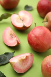 Photo of Tasty apples with red pulp and leaves on light green background, closeup