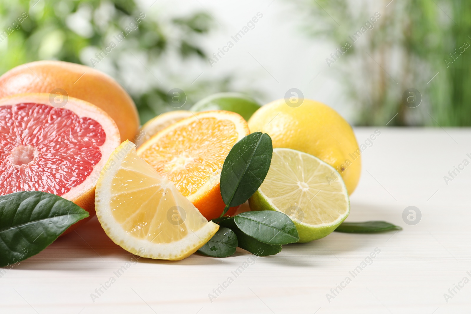 Photo of Different cut and whole citrus fruits on white wooden table, closeup. Space for text