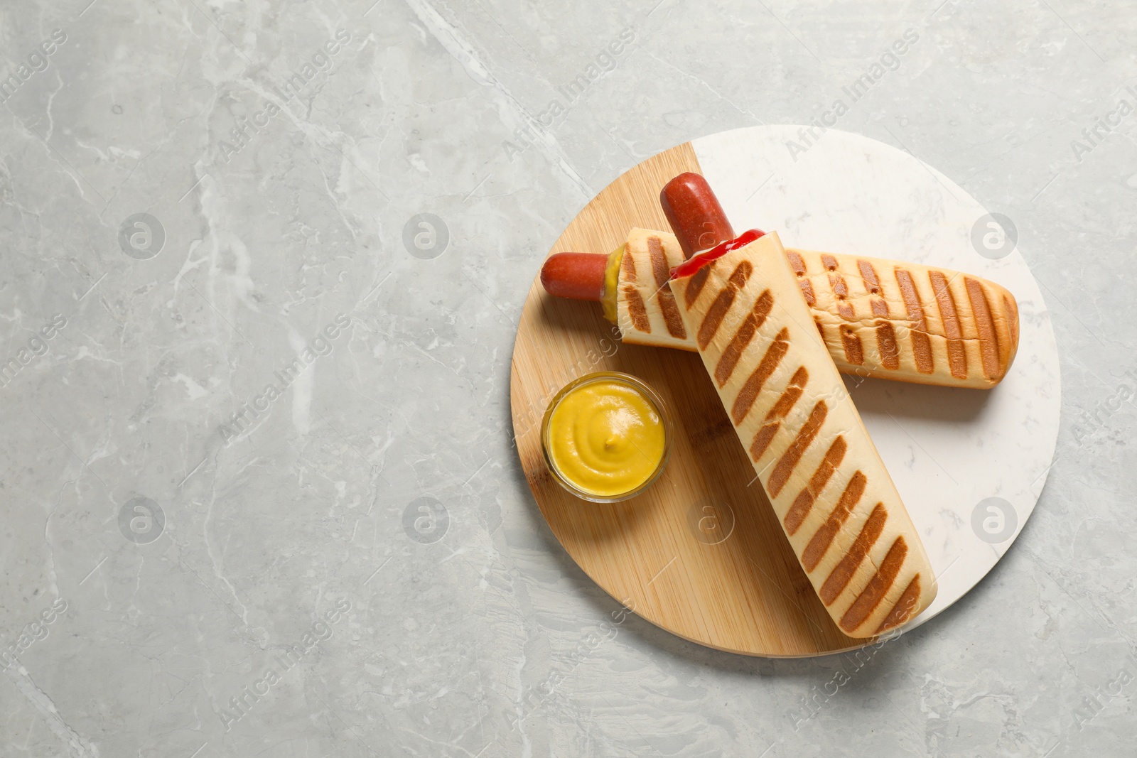 Photo of Tasty french hot dogs and dip sauce on light grey marble table, top view. Space for text