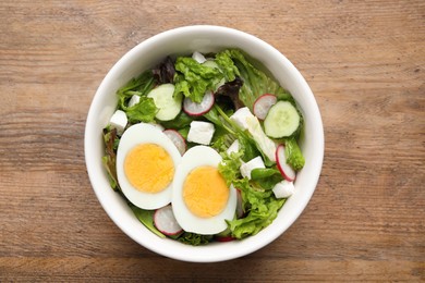 Photo of Delicious salad with boiled egg, feta cheese and vegetables on wooden table, top view
