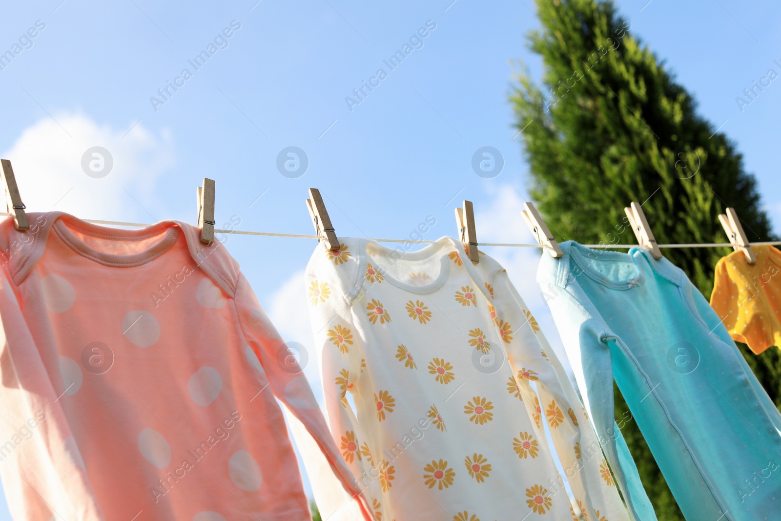 Photo of Clean baby onesies hanging on washing line in garden. Drying clothes