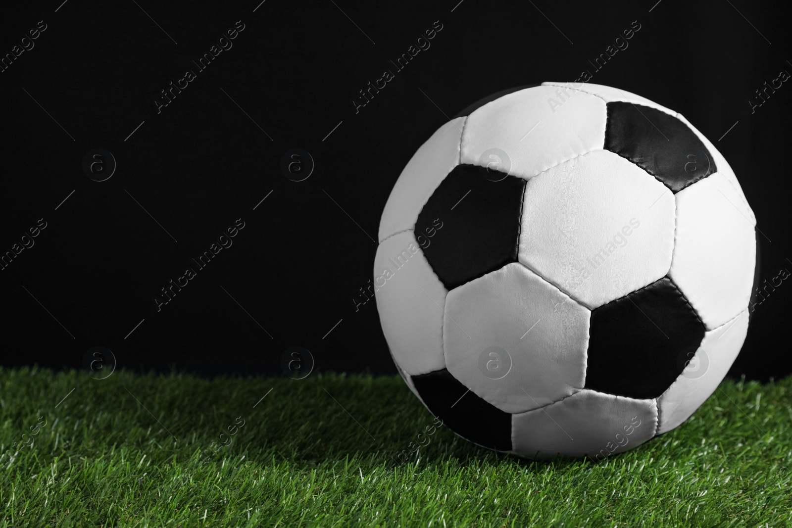 Photo of Football ball on green grass against black background. Space for text