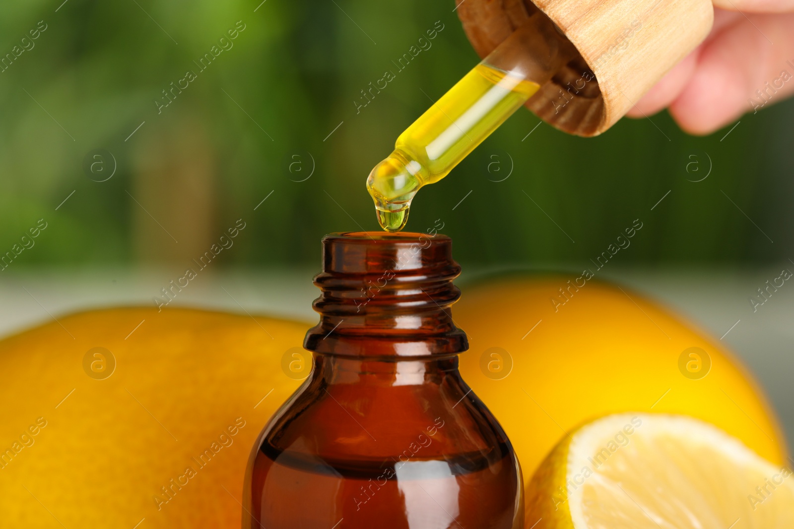 Photo of Woman dripping essential oil into bottle against blurred background, closeup