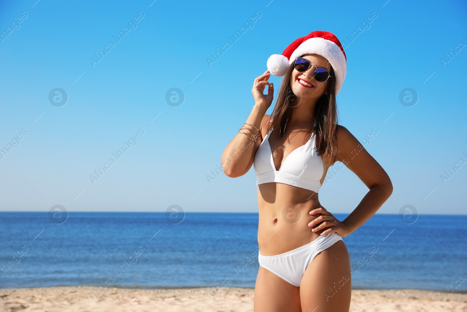 Photo of Young woman wearing Santa hat and bikini on beach, space for text. Christmas vacation