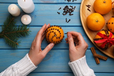 Woman decorating fresh tangerine with cloves at light blue wooden table, top view