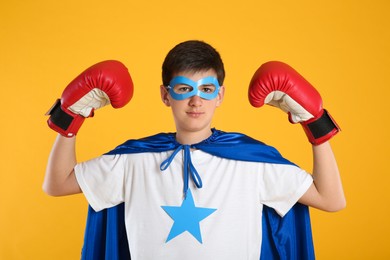 Teenage boy in superhero costume on yellow background