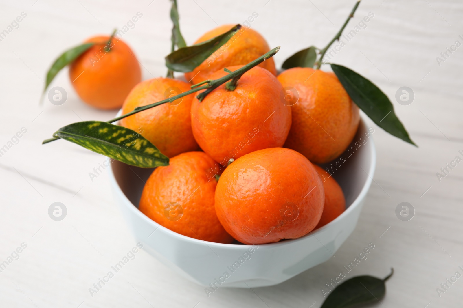 Photo of Bowl with fresh ripe tangerines and leaves on white table