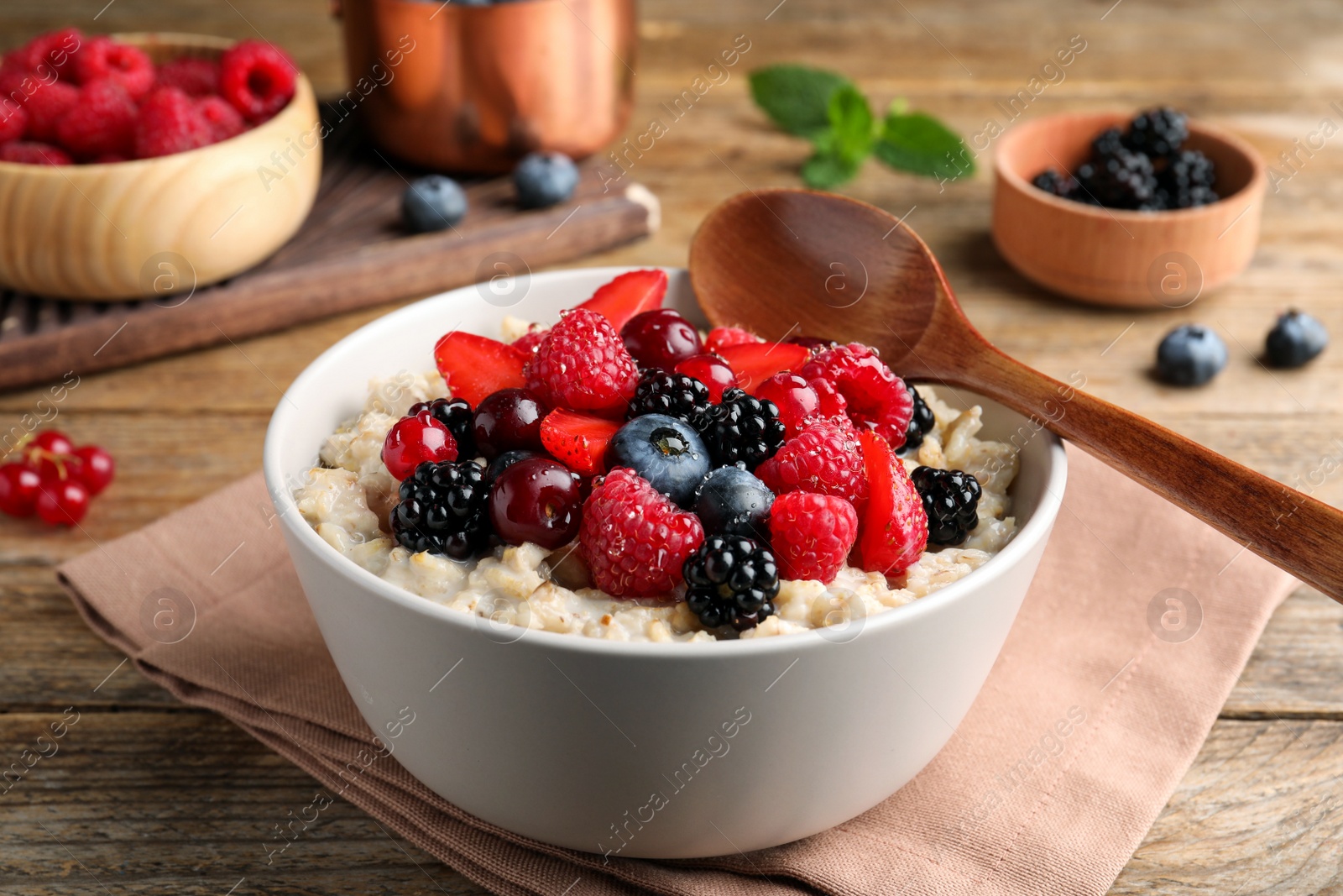 Photo of Bowl with tasty oatmeal porridge and berries served on wooden table. Healthy meal