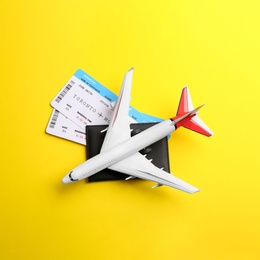 Toy airplane and passport with tickets on yellow background, flat lay