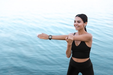 Photo of Young sportswoman with wireless earphones stretching near river