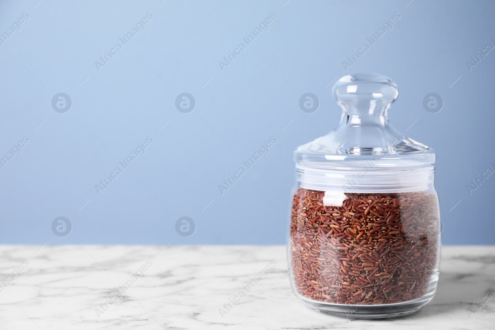 Photo of Brown rice in jar on white marble table. Space for text