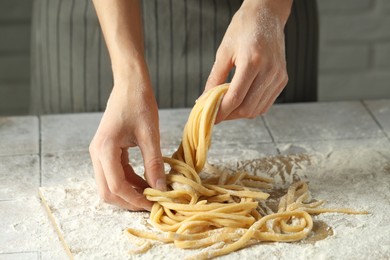 Photo of Woman with homemade pasta at light tiled table, closeup