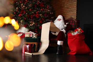 Santa Claus reading wish list in armchair near Christmas tree