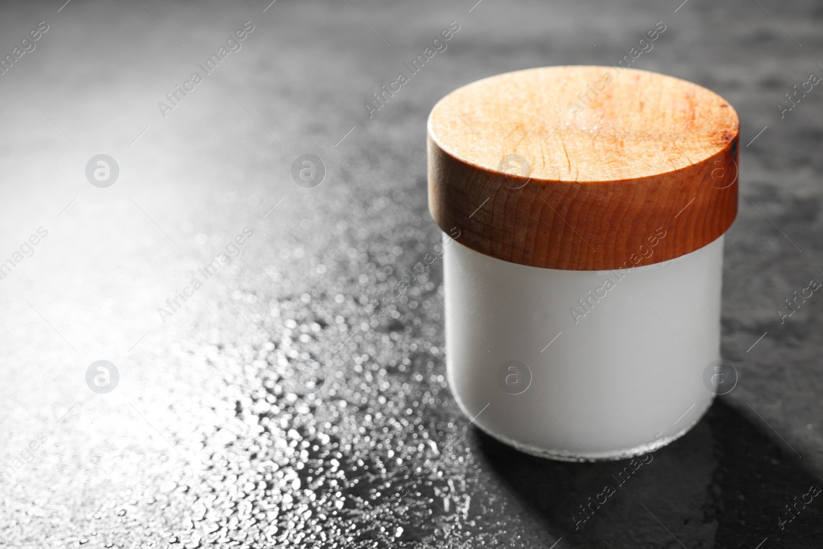 Photo of Jar of cosmetic product on wet grey table, closeup. Space for text