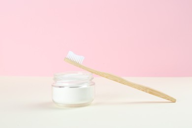 Bamboo toothbrush and bowl of baking soda on beige table against pink background