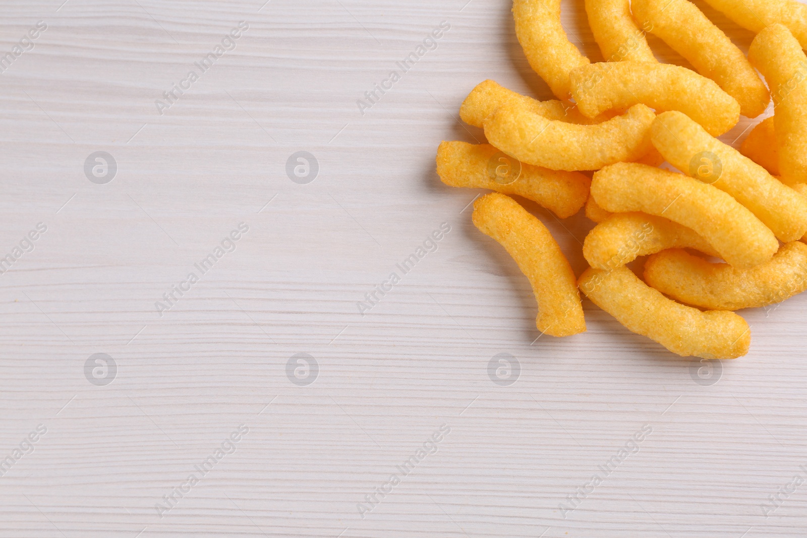 Photo of Heap of tasty cheesy corn puffs on white wooden table, flat lay. Space for text