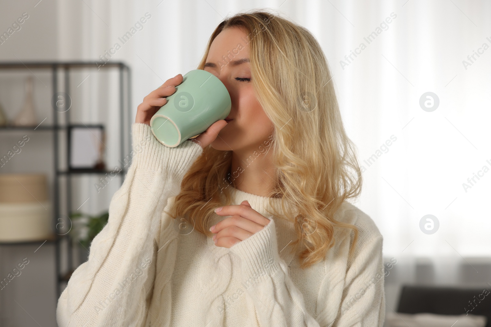 Photo of Beautiful woman in stylish warm sweater drinking tea at home