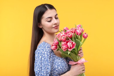 Happy young woman with beautiful bouquet on orange background