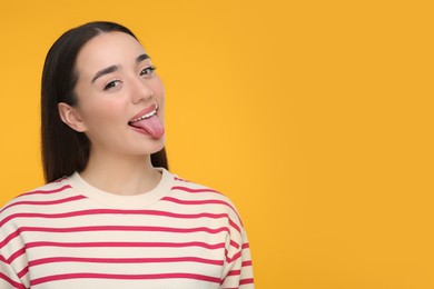 Happy woman showing her tongue on orange background, space for text