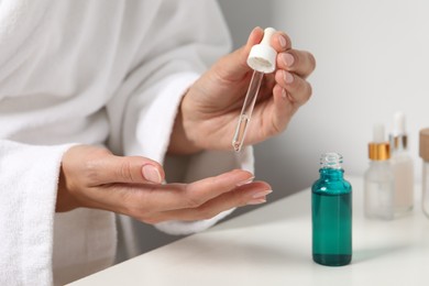 Woman applying cosmetic serum onto her finger at white table, closeup