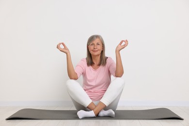 Happy senior woman practicing yoga on mat near white wall