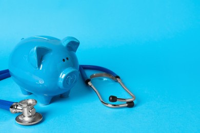 Photo of Ceramic piggy bank and stethoscope on light blue background, space for text. Medical insurance