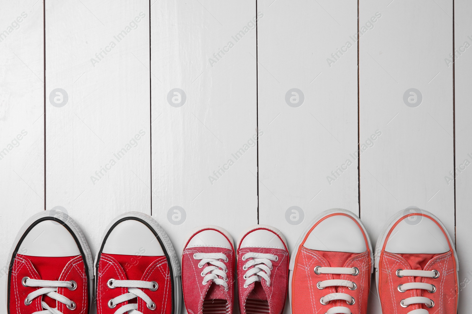 Photo of Stylish sneakers for all family members on white wooden background, flat lay