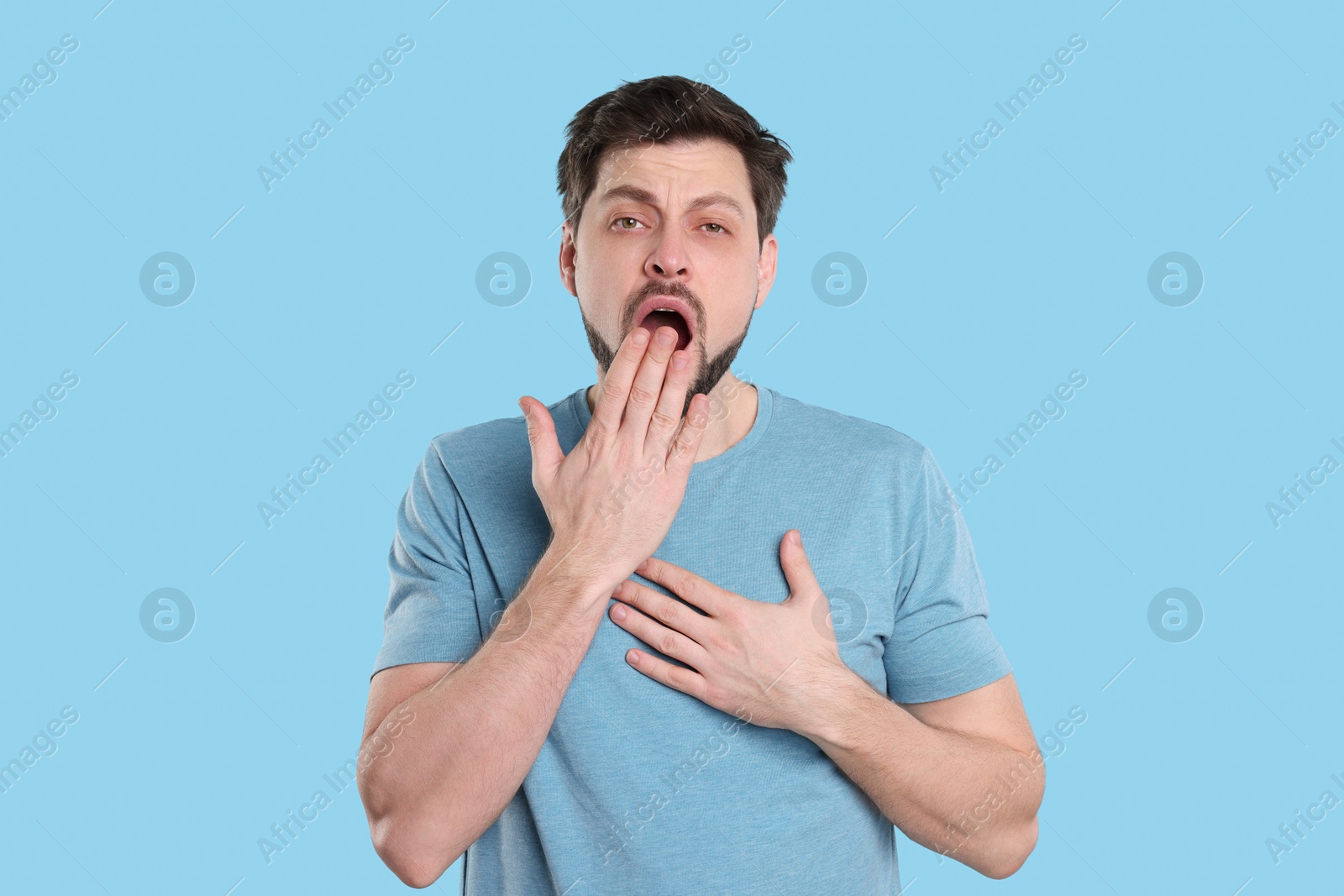 Photo of Tired man yawning on light blue background. Insomnia problem