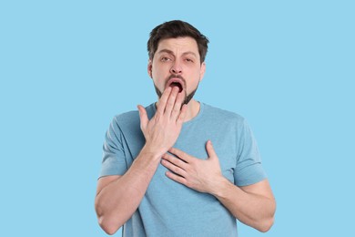 Photo of Tired man yawning on light blue background. Insomnia problem