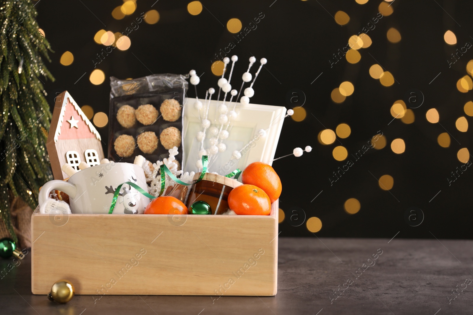 Photo of Wooden crate with Christmas gift set on grey table against festive lights. Space for text