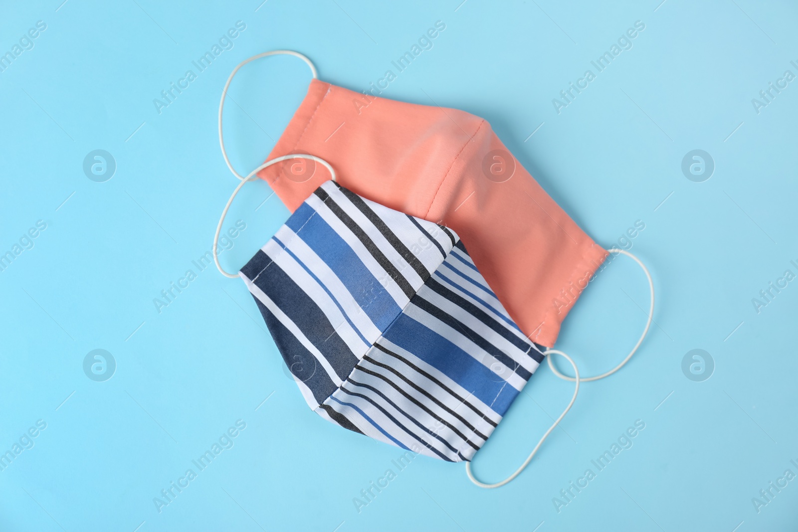 Photo of Homemade protective face masks on light blue background, flat lay