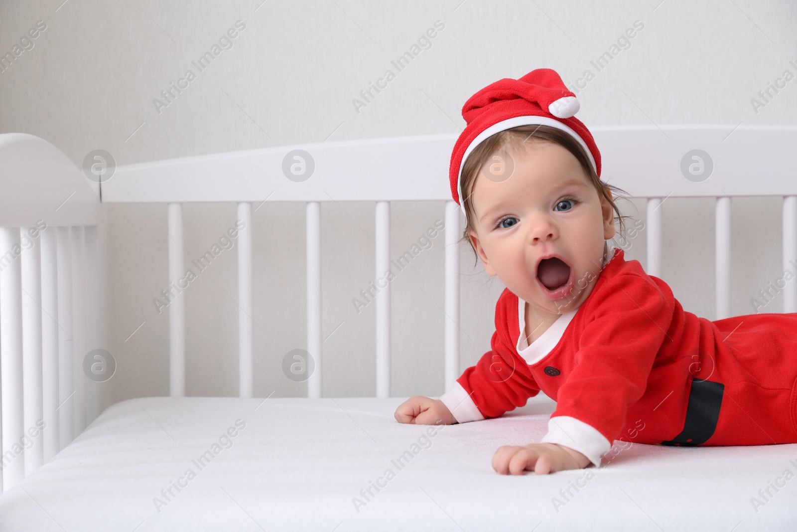 Photo of Cute baby wearing festive Christmas costume in crib. Space for text