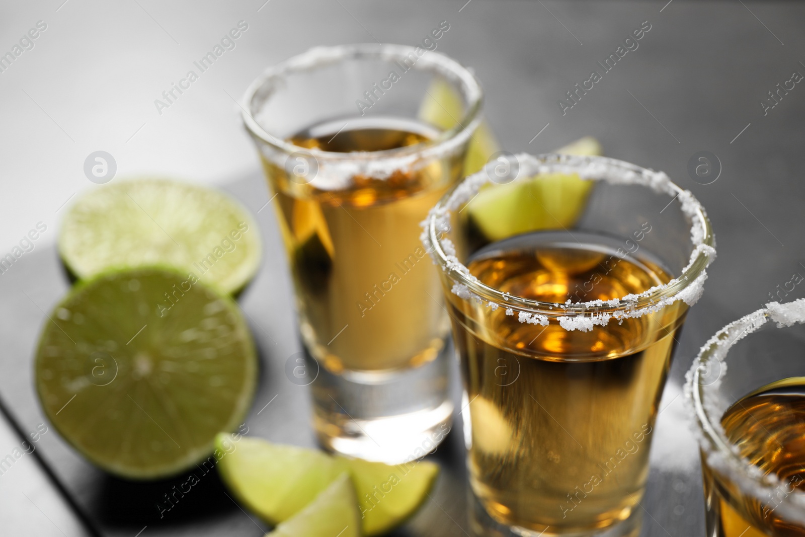 Photo of Mexican Tequila shots with salt and lime slices on grey table, closeup