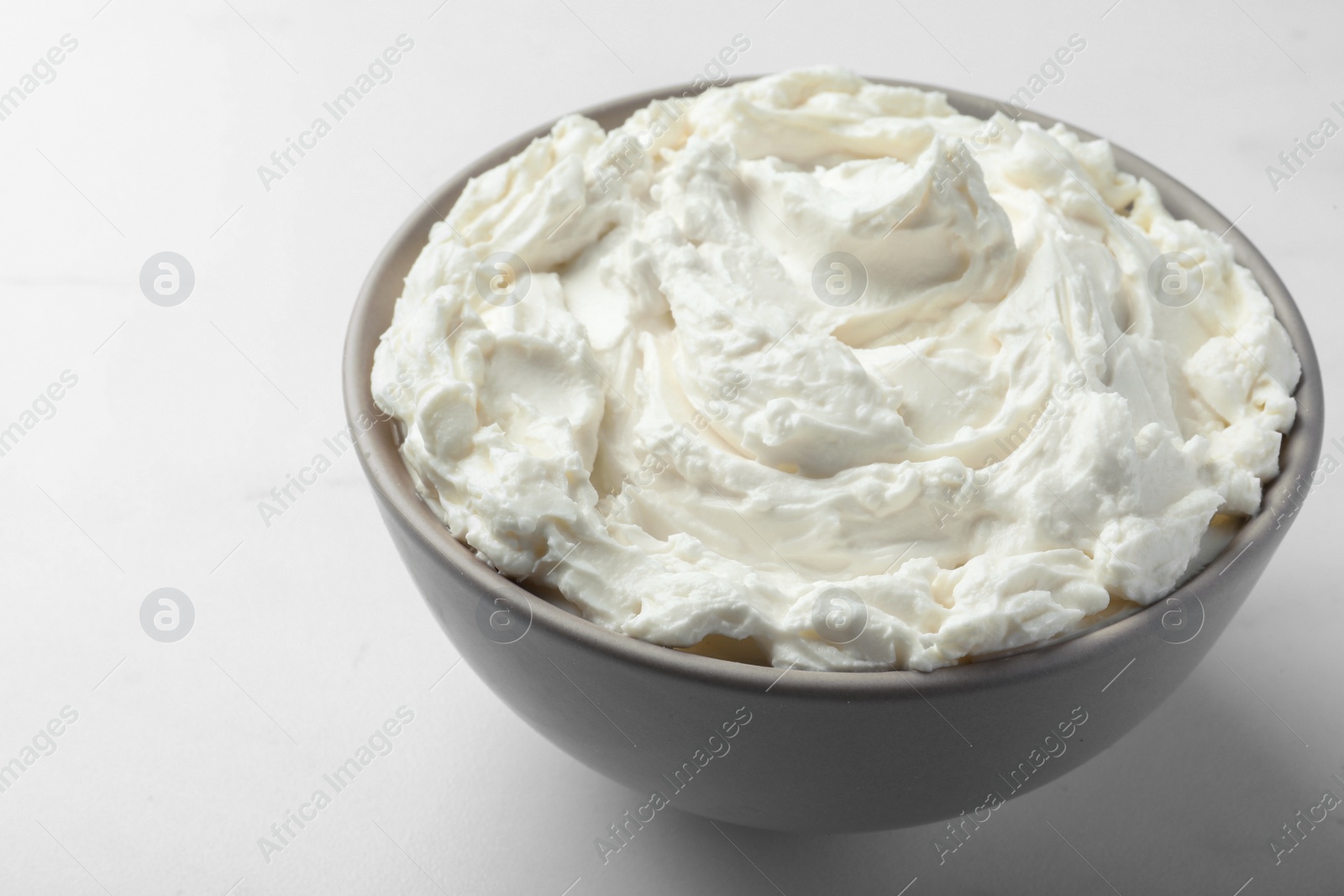 Photo of Bowl of tasty cream cheese on white table, closeup