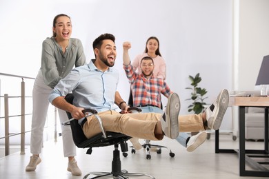 Happy office employees riding chairs at workplace