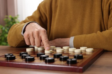 Photo of Playing checkers. Senior man thinking about next move at table in room, closeup