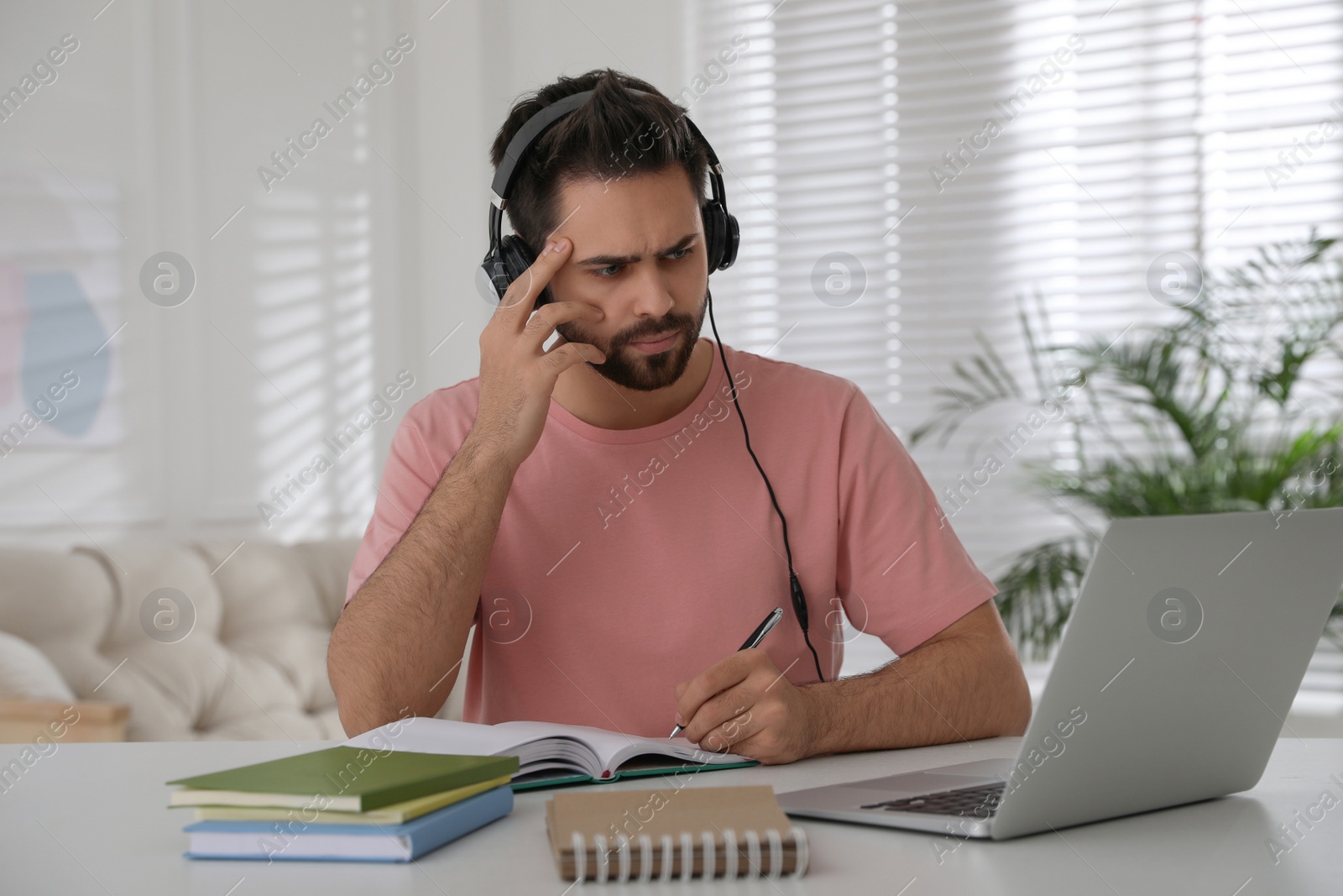 Photo of Confused young man watching webinar at table in room