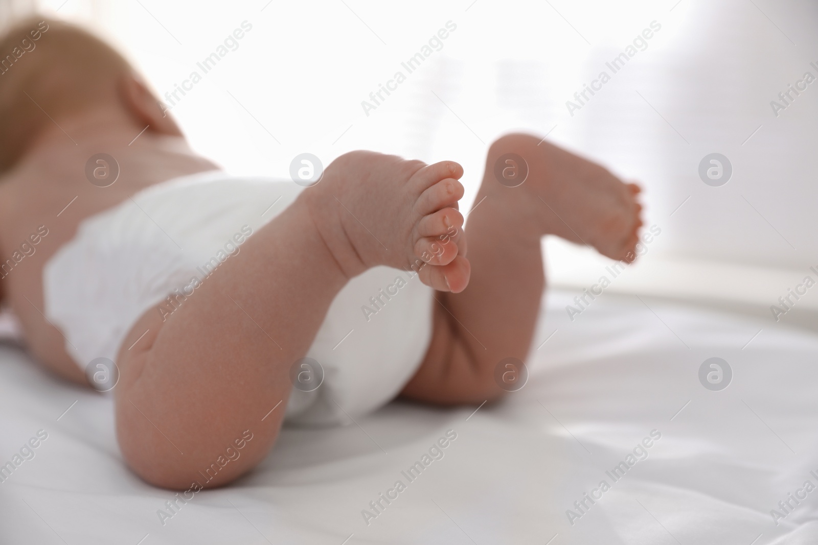 Photo of Cute little baby in diaper on bed, closeup