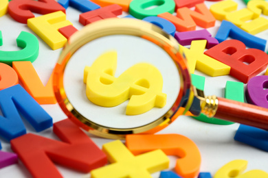 Photo of Magnifying glass over dollar sign surrounded by magnet letters on white background, closeup. Search concept