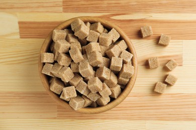 Photo of Brown sugar cubes in bowl on wooden table, top view