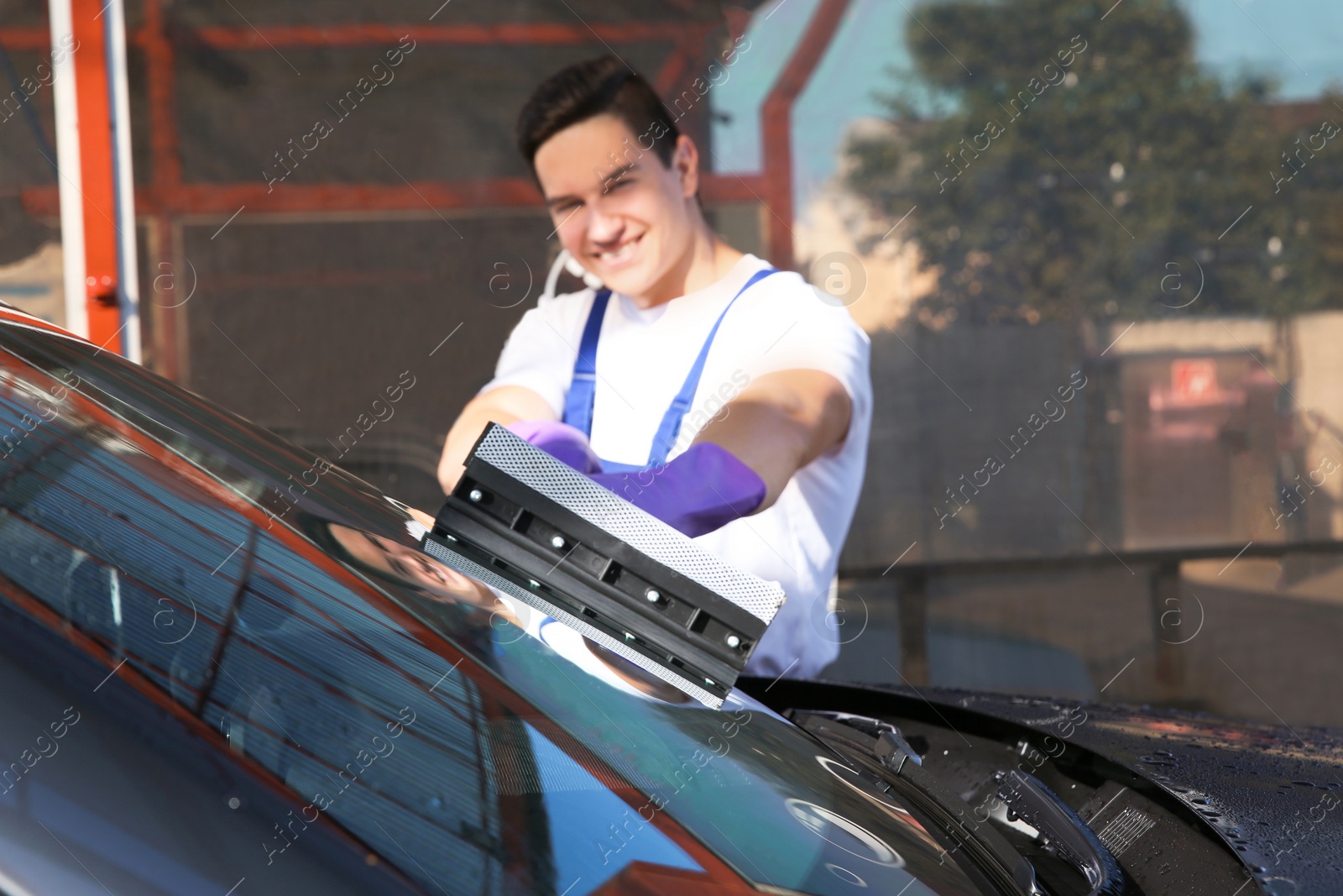 Photo of Worker cleaning automobile windshield with squeegee at car wash