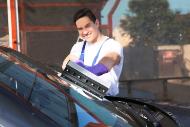 Photo of Worker cleaning automobile windshield with squeegee at car wash