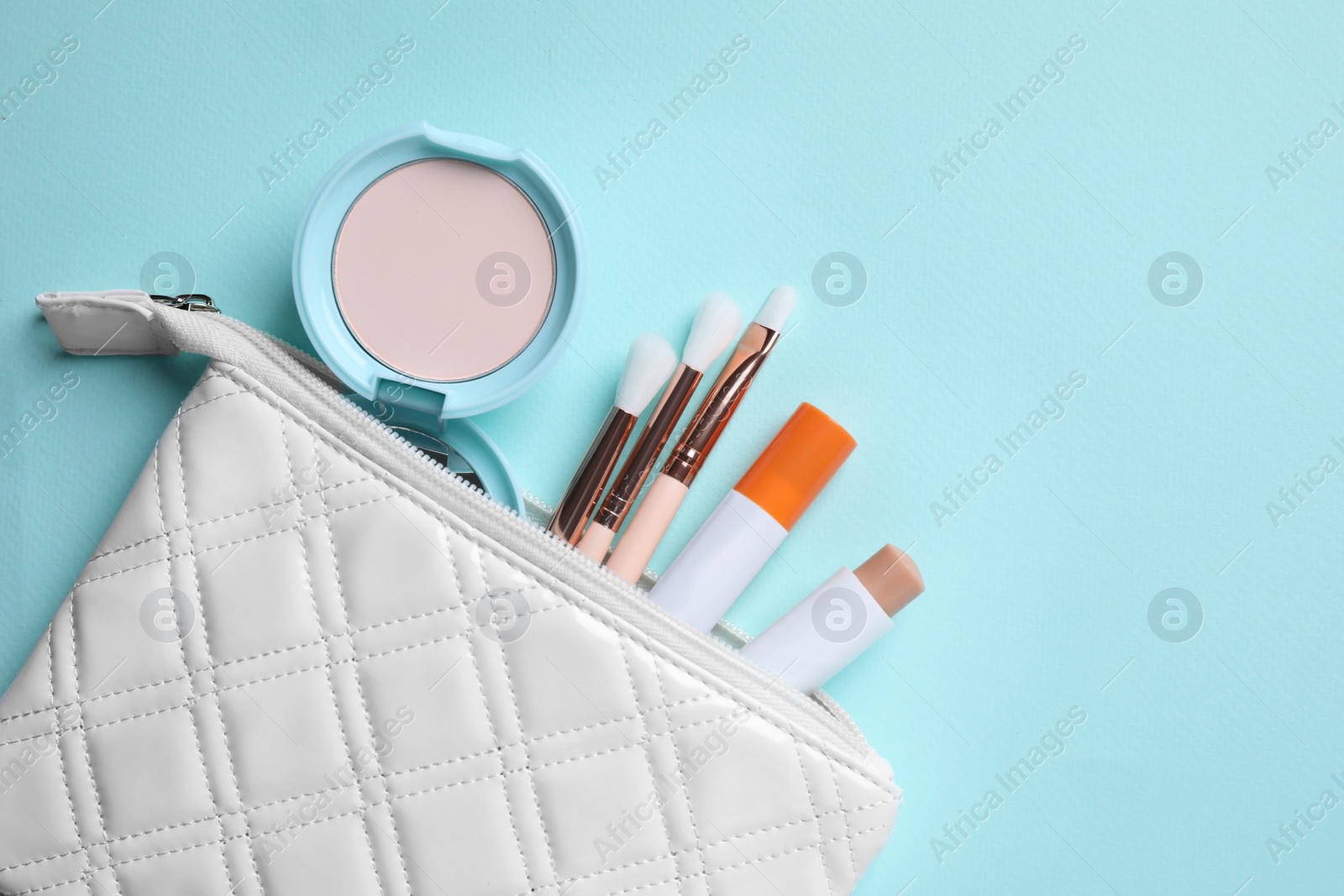 Photo of Bag with hygienic lipstick and cosmetic products on turquoise background, flat lay